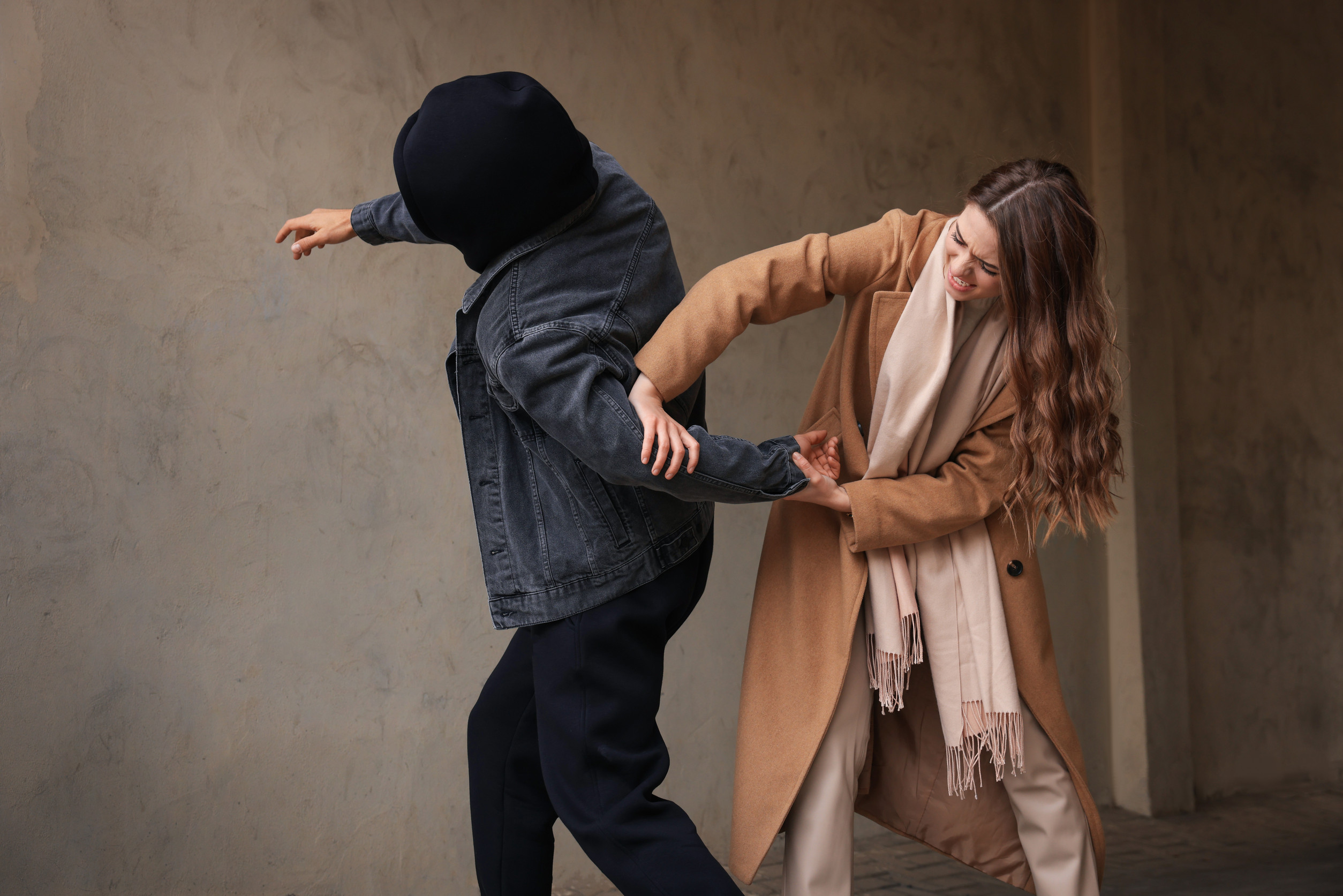 Woman defending herself from attacker near beige wall outdoors